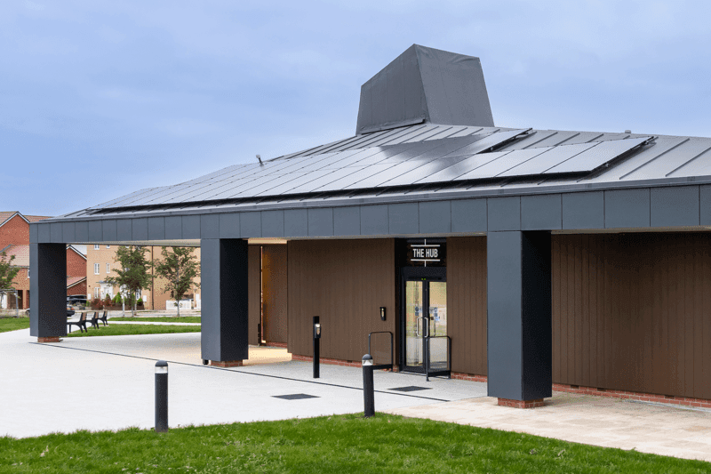 Modern building with a flat roof and solar panels, featuring a glass entrance and landscaped lawn in front.