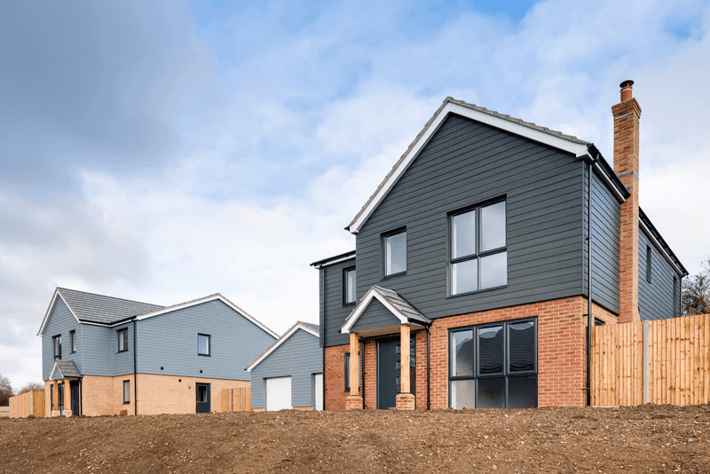 Deux maisons modernes sur un terrain, l'une avec un extérieur noir et des accents de briques, l'autre bleu clair, avec un ciel clair en arrière-plan.