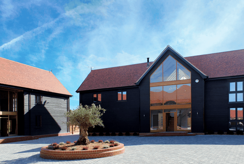 Modern black building with a large glass entrance, surrounded by a landscaped courtyard and a blue sky.